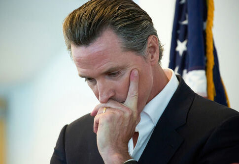 Man in suit thinking with hand on face near a U.S. flag