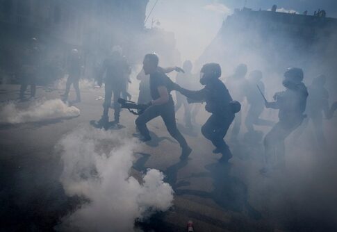 Riot police engaging with protesters amidst clouds of tear gas